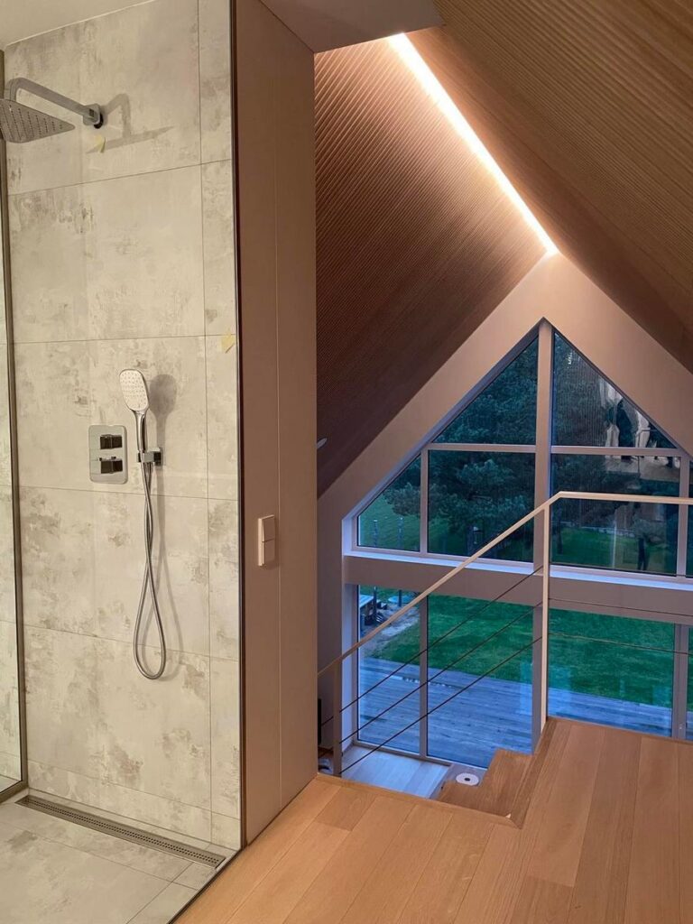 Apšvietimu pabrėžiamas patalpos aukštis, lubų faktūra ir stogo forma.